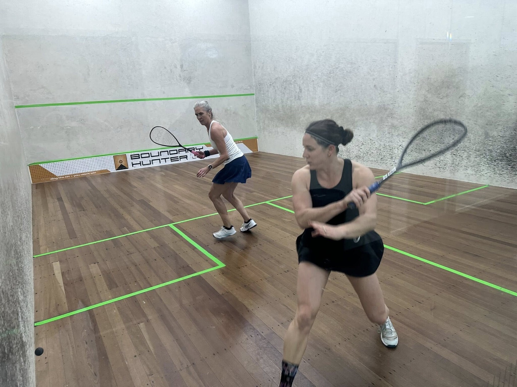 Two members playing on a glass backed court